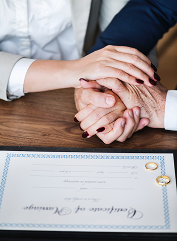 Couple holding hands while signing marriage certificate with wedding bands